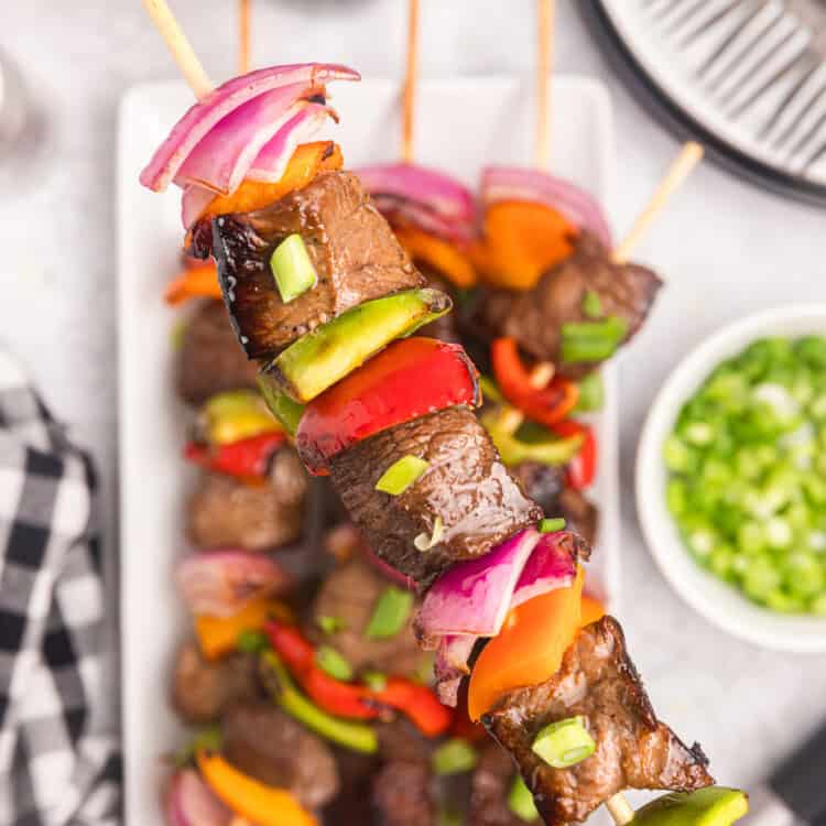 Blackstone Beef Kabobs arranged on serving plate, holding on kabob up close