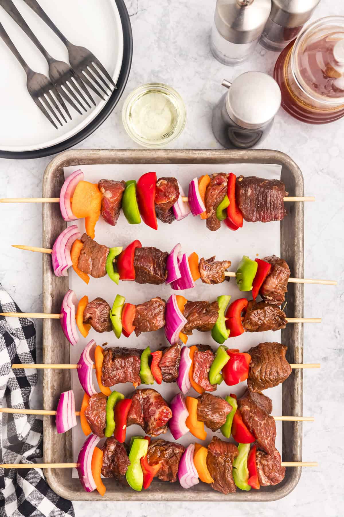 Assembling marinaded meat and fresh peppers and onion chunks on wooden kabob stick over parchment lined cooking sheet for Blackstone Beef Kabobs recipe