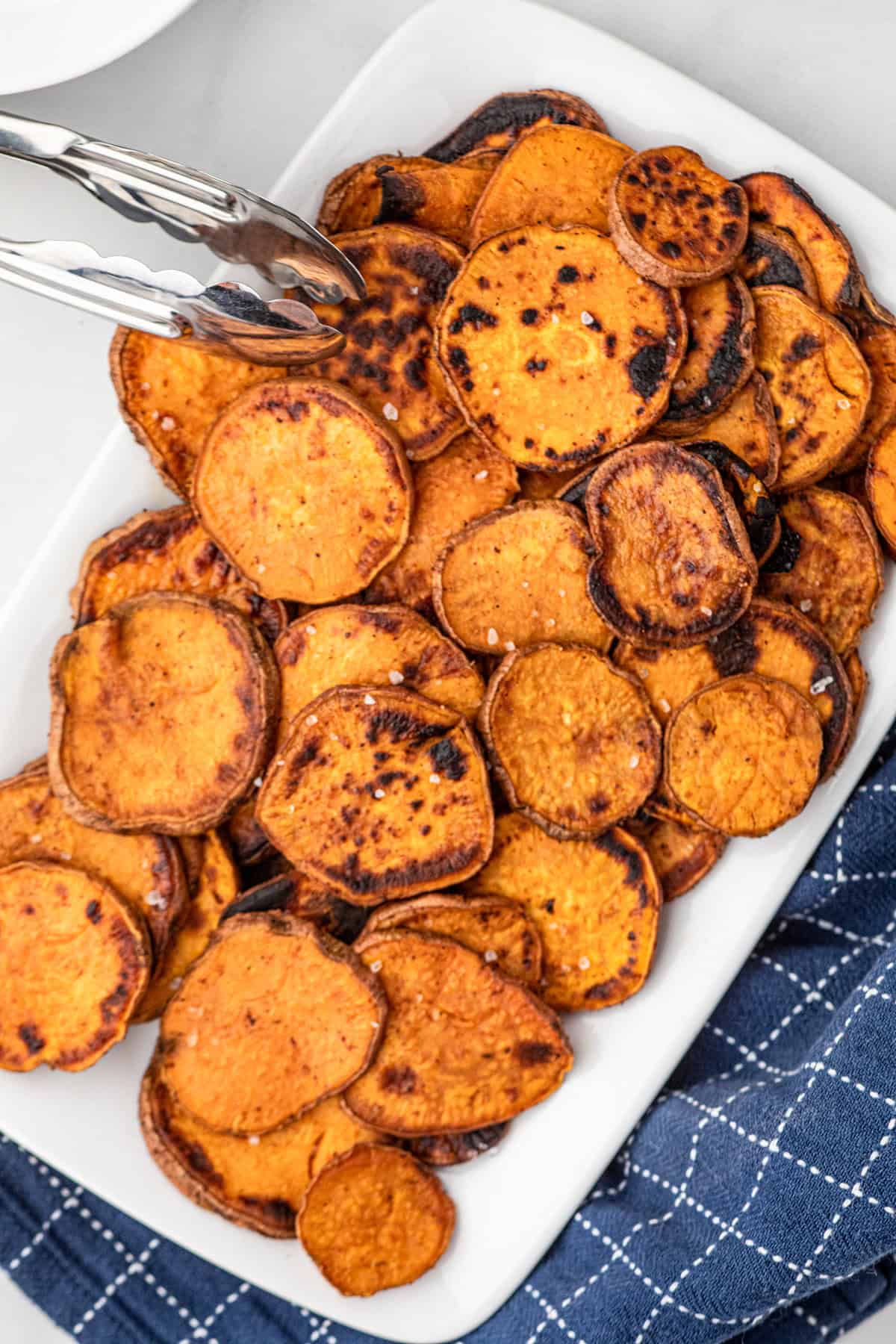 Grilled Sweet Potatoes arranged on serving place and using a tongs to lift from plate