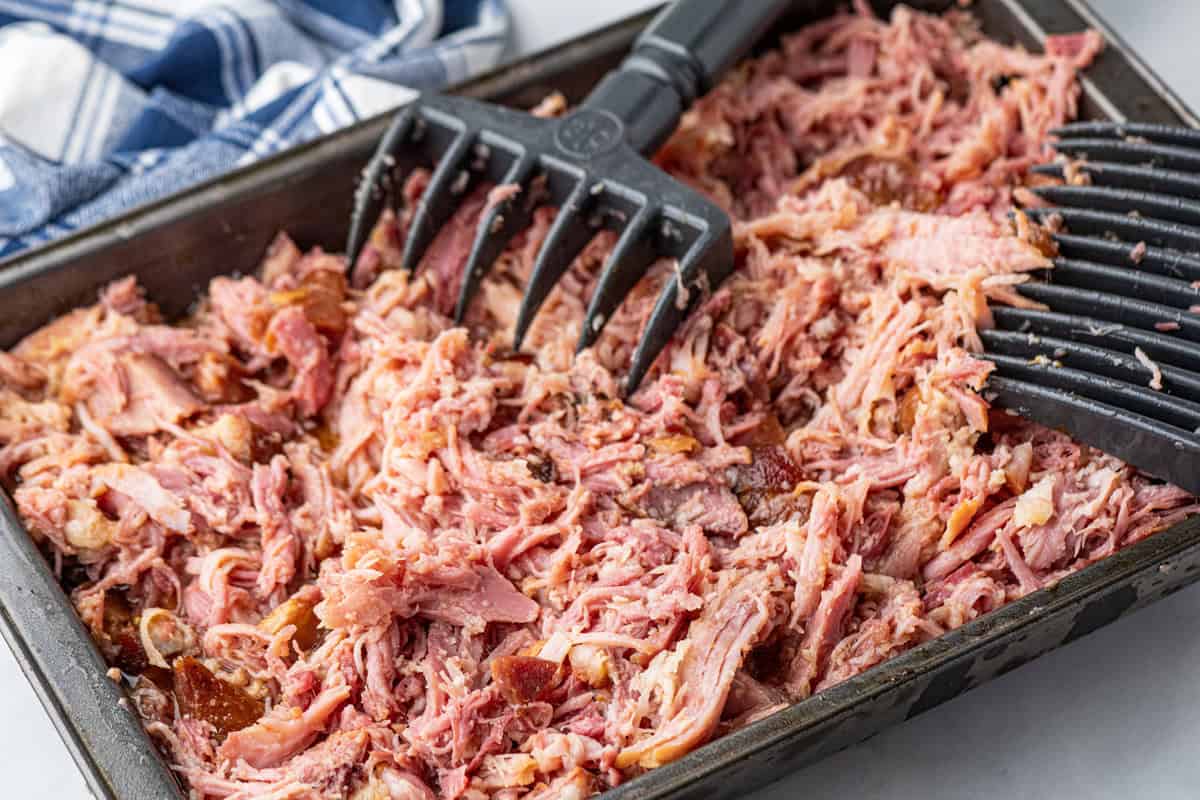 Smoked pulled ham in shallow baking dish being shredded