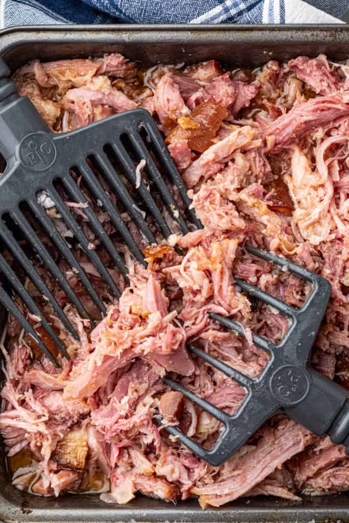 Shredding Pulled Pork Ham in pan with large  meat shredders