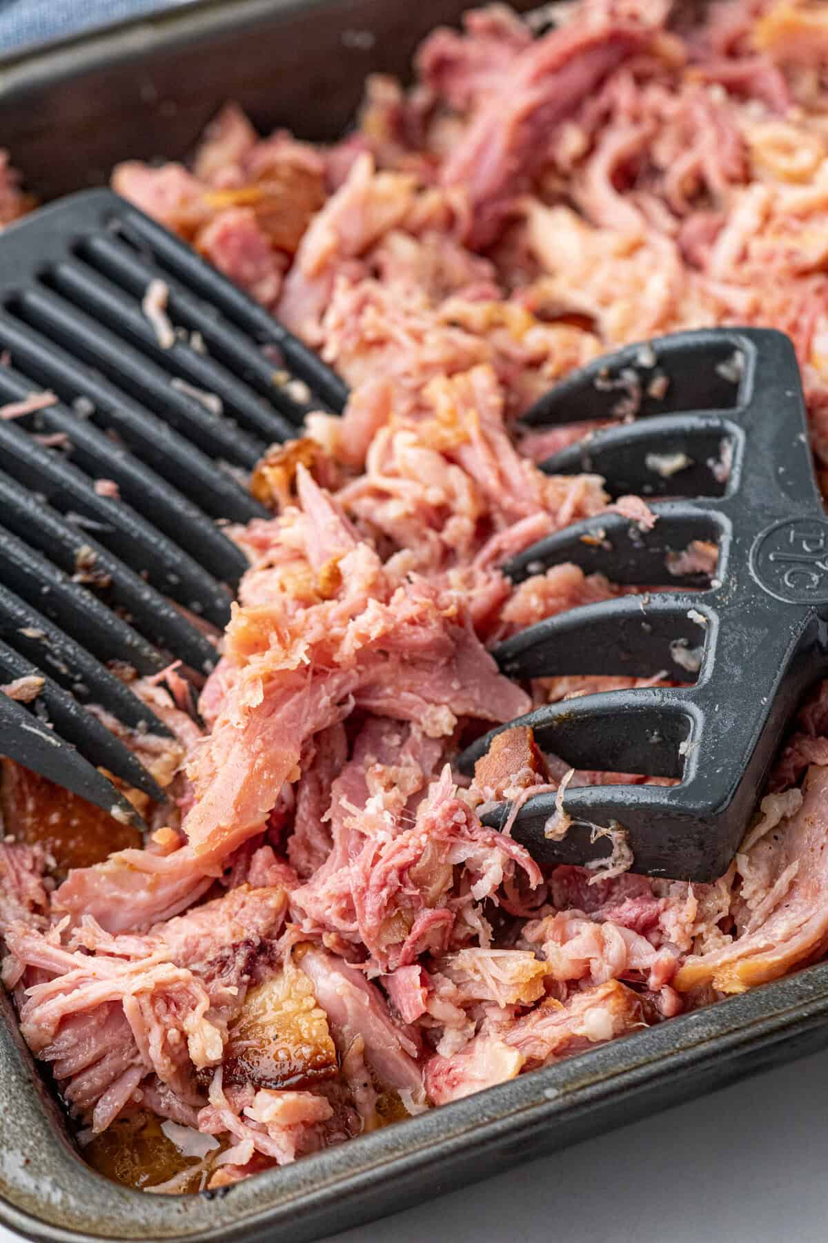 Pulled Pork Ham in cooking pan being pulled apart