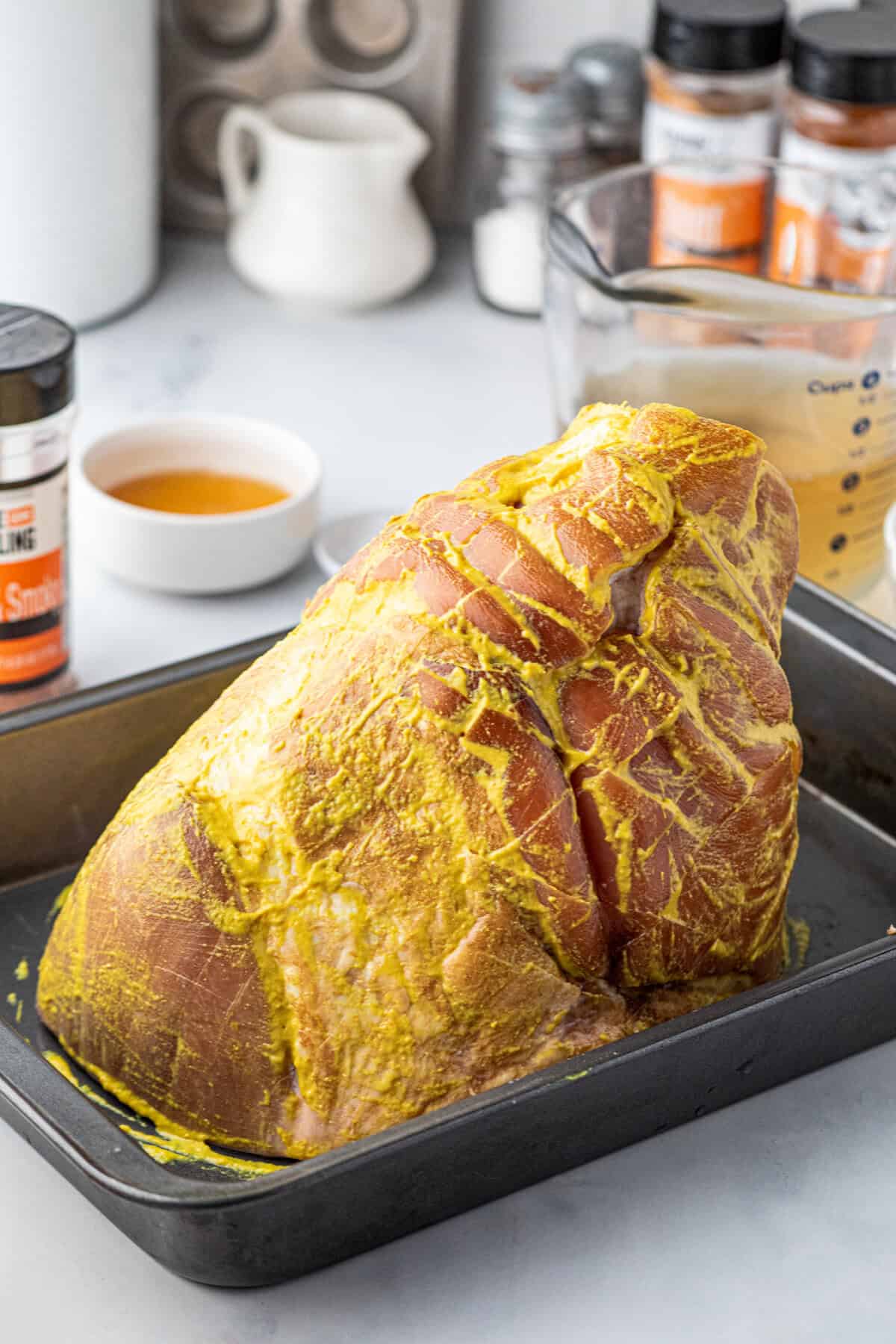Lathering whole picnic ham with yellow mustard prior to seasoning in shallow baking pan