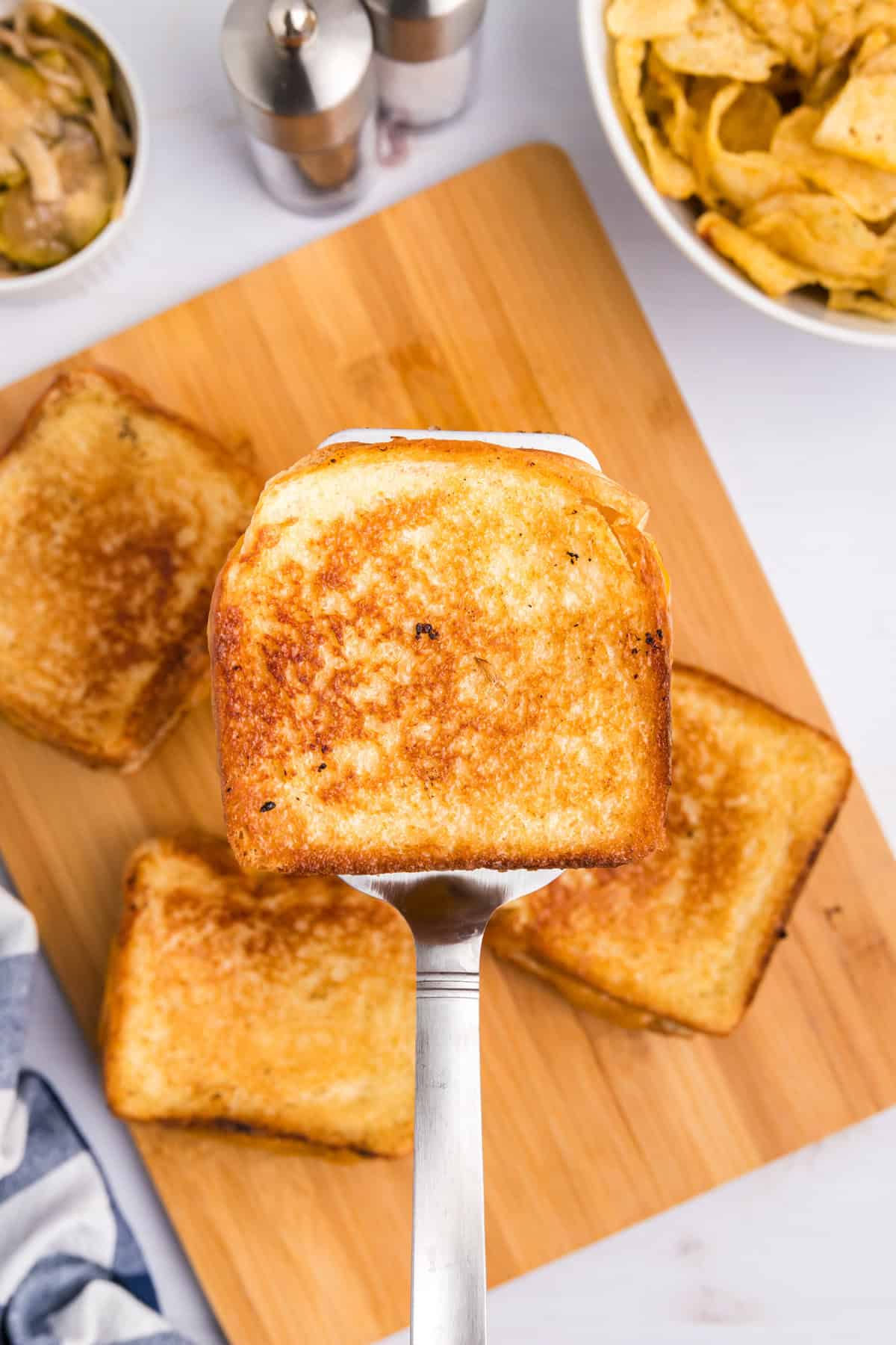 Using metal spatula to lift a Blackstone Grilled Cheese from stack on wood serving tray