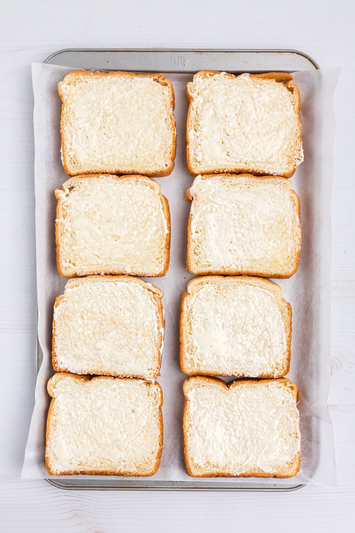 Tray lined with bread pieces smeared with mayonaise for Blackstone Grilled Cheese recipe