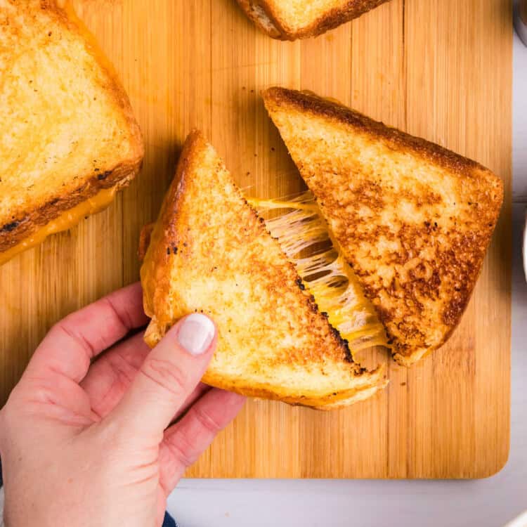 Closeup square image of Blackstone Grilled Cheese being pulled apart on wood tray