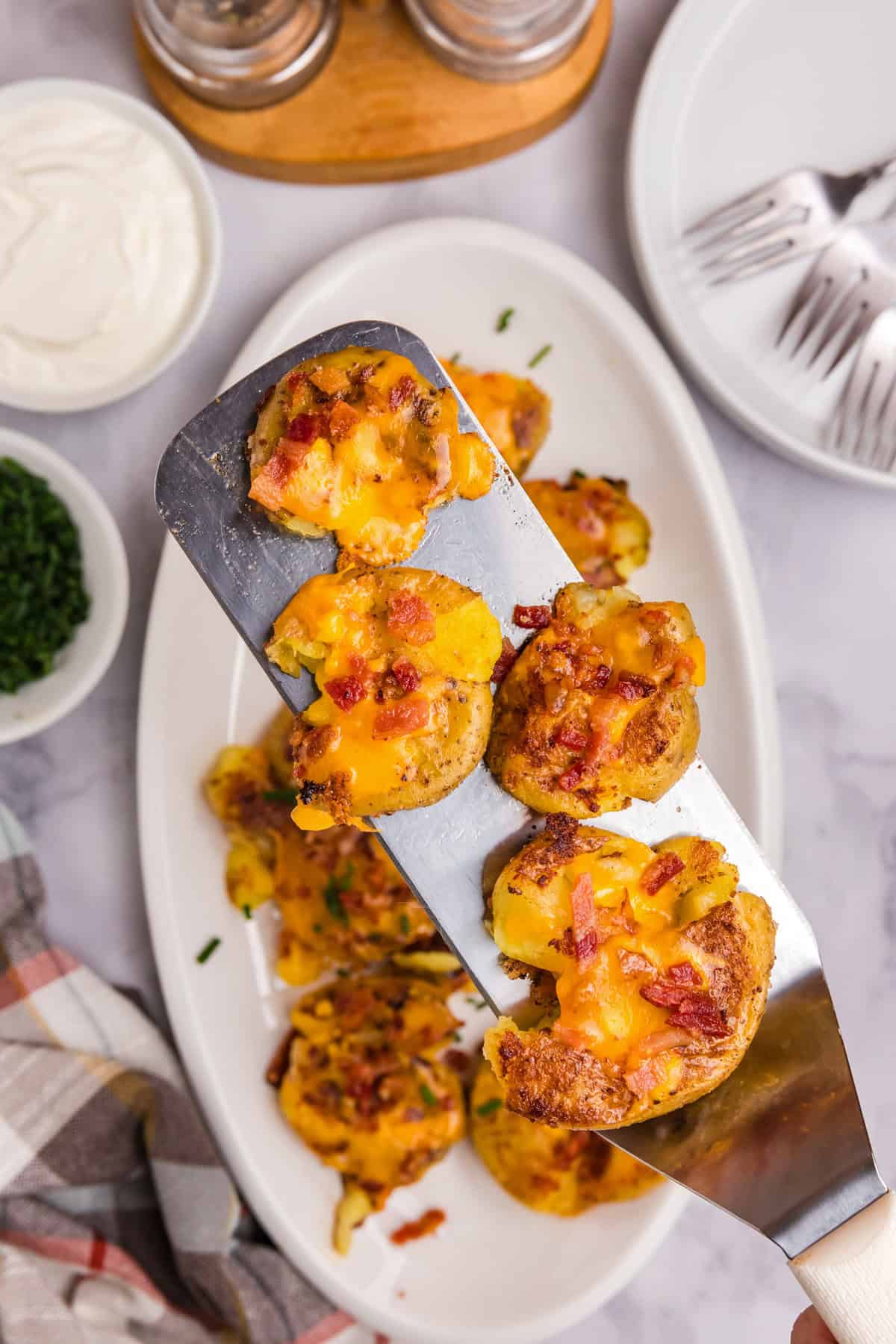Using grilling spatula to lift Blackstone Loaded Smashed Potatoes from serving plate
