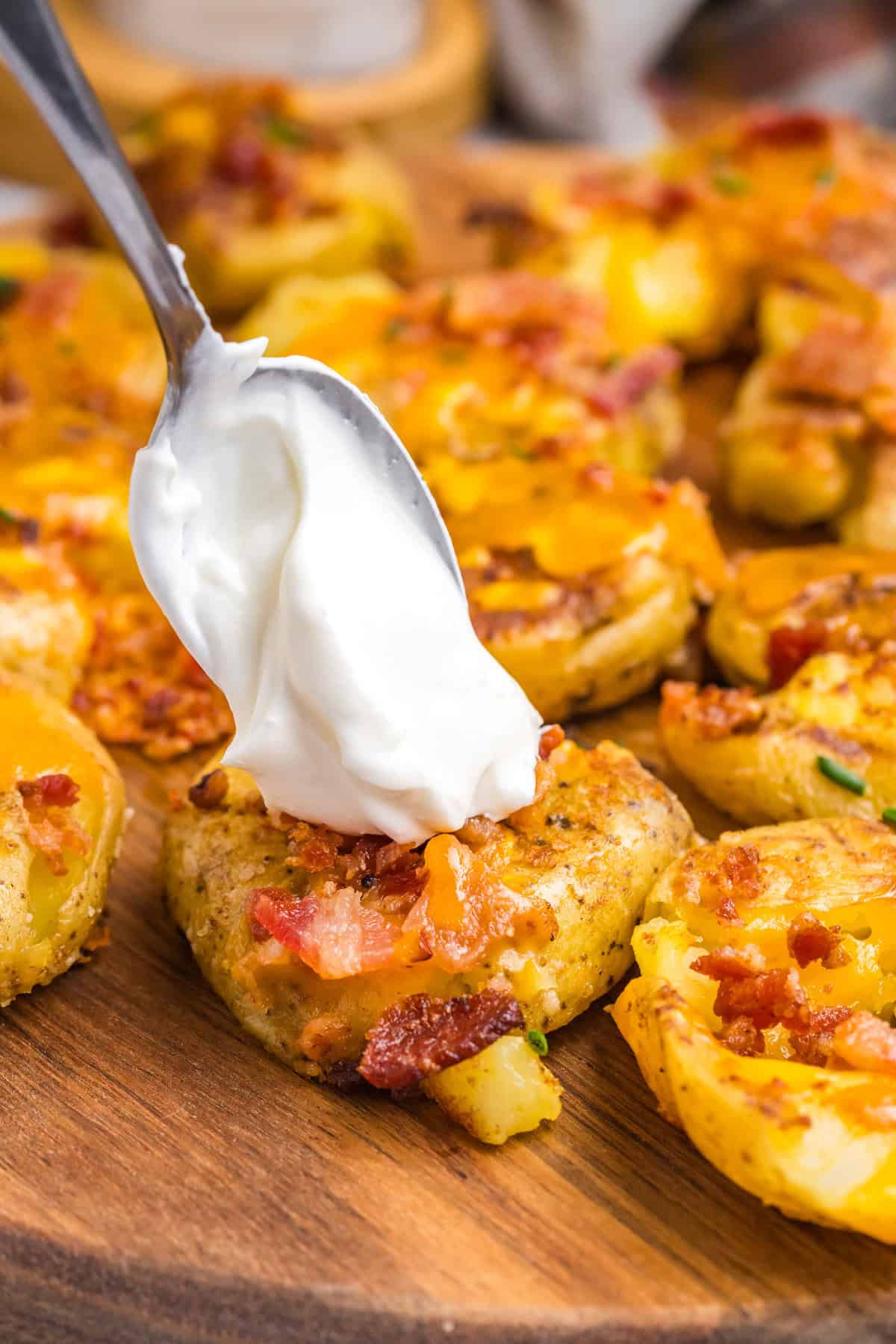 Adding a dollop of sour cream with spoon to Blackstone Loaded Smashed Potatoes