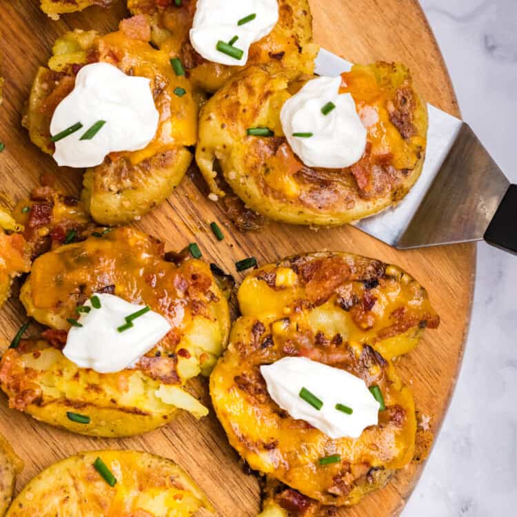 Blackstone Loaded Smashed Potatoes on wood serving board using a spatula to lift one piece