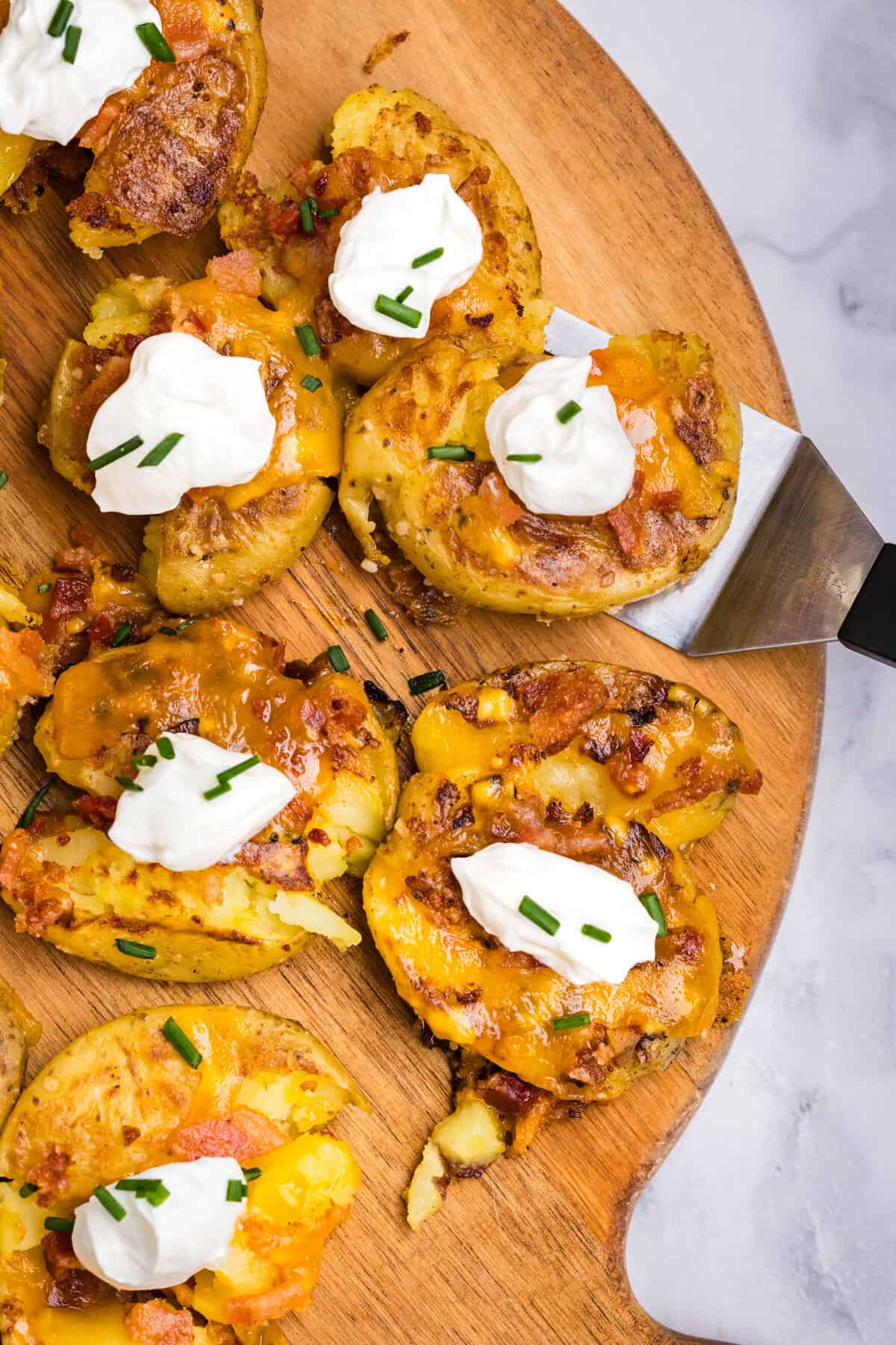 Blackstone Loaded Smashed Potatoes on wood serving board using a spatula to lift one piece