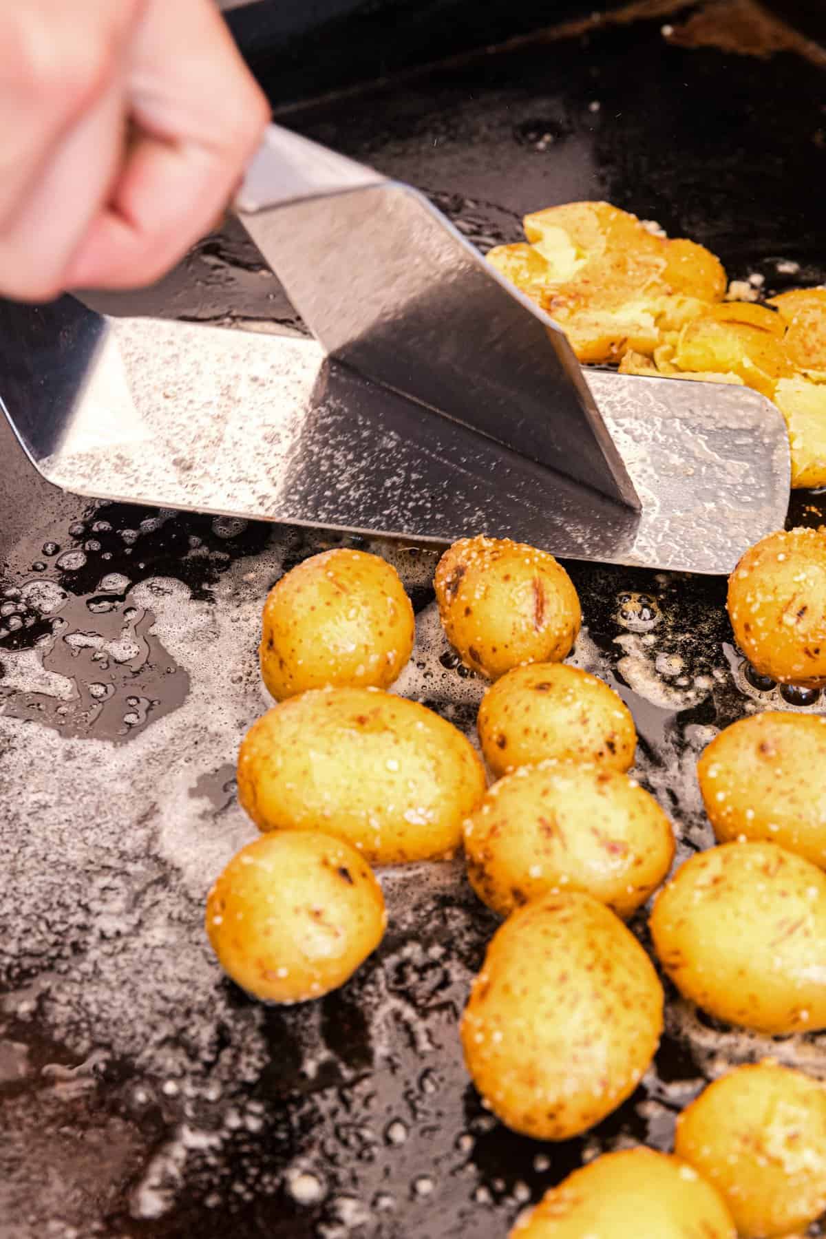 Smashing potatoes on Blackstone with grilling spatula for Loaded Smashed Potatoes recipe
