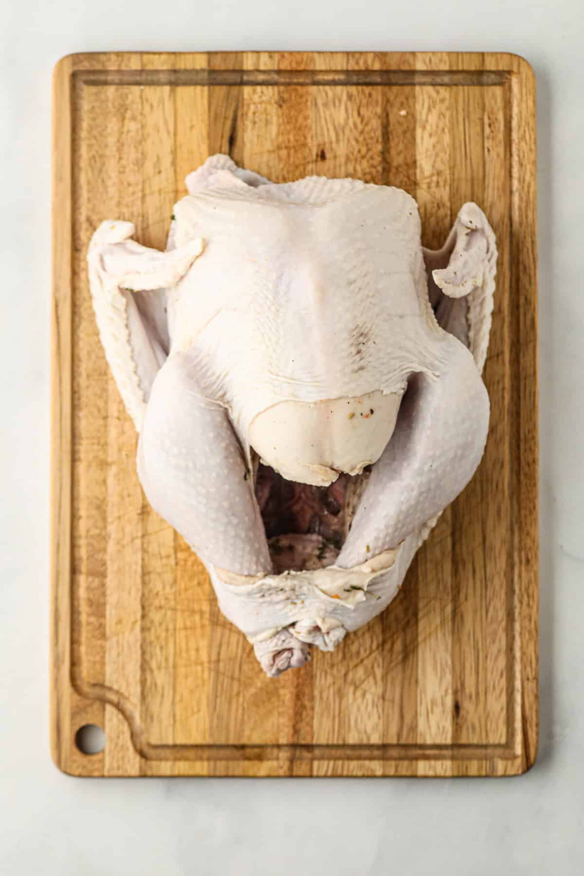 Overhead picture of partially cooked turkey on wooden cutting board.