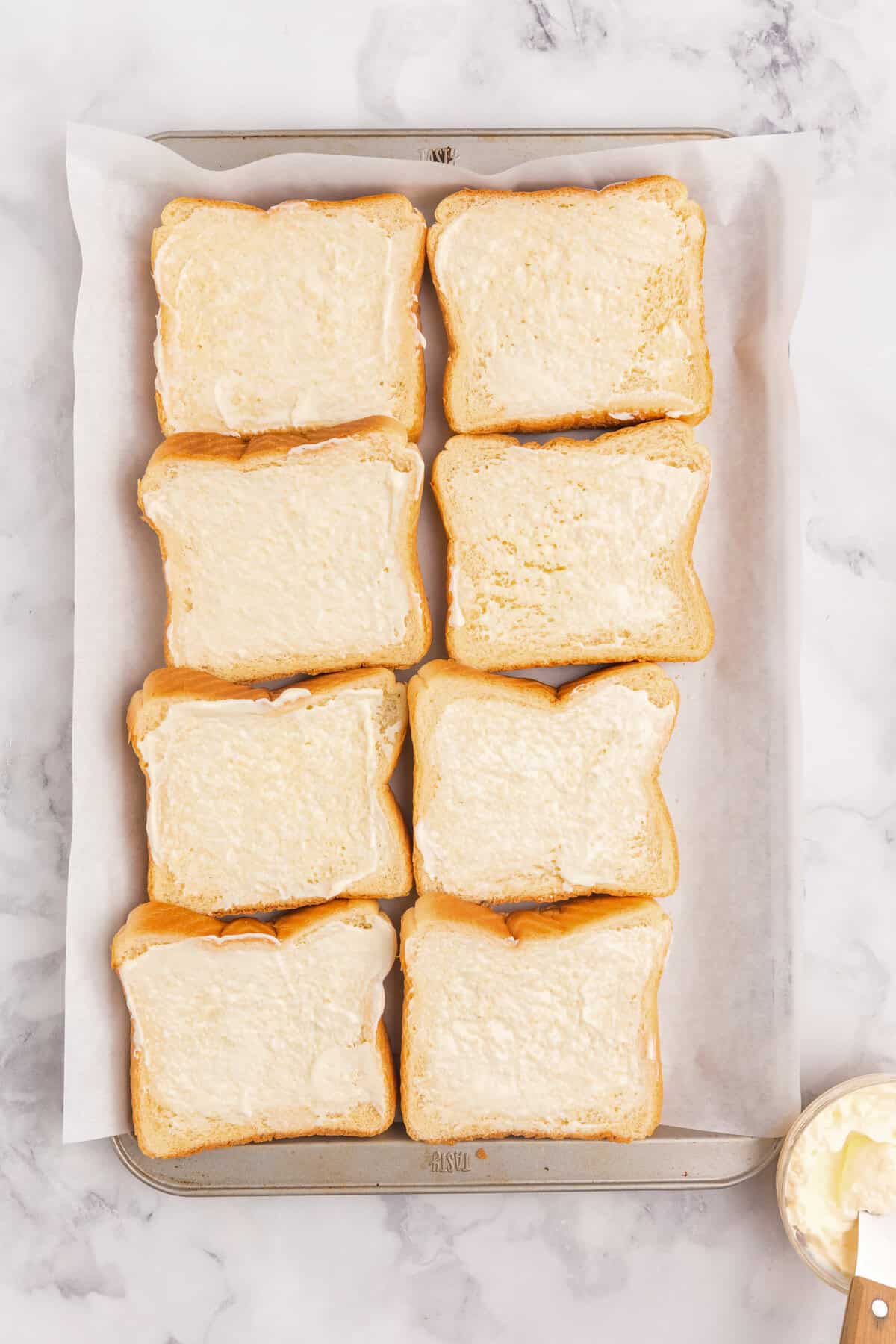 Overhead picture of a parchment paper lined pan with bread with mayonnaise on them in it.