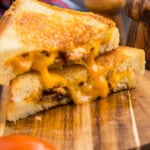 Completed grilled cheese cut in half and stacked on top of each other on a wooden cutting board.