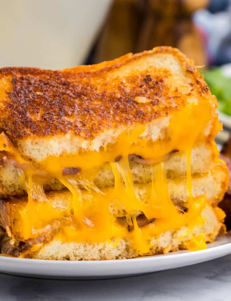 White plate with completed grilled cheese cut in half on it.