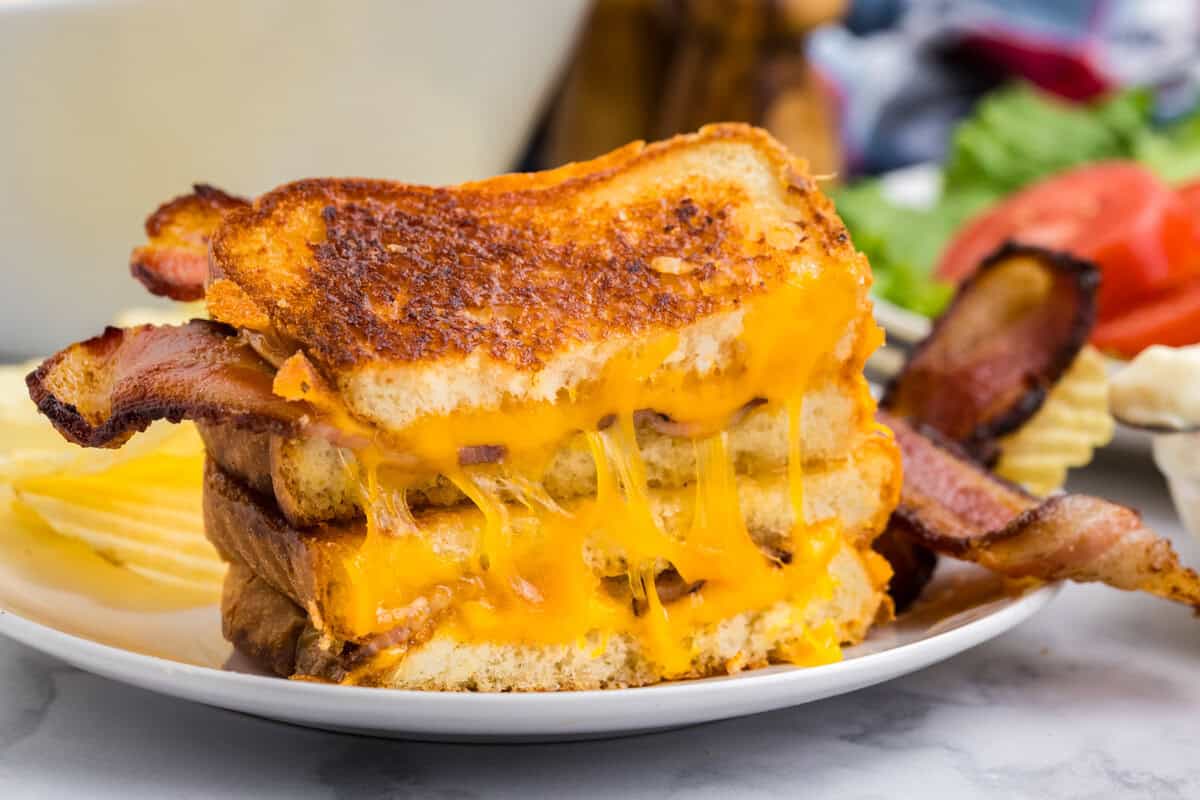 White plate with completed grilled cheese cut in half on it.