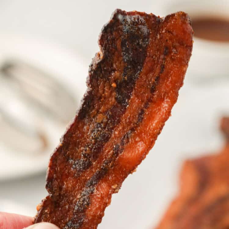 Picture of hand holding up a single piece of completed Smoked Candied Bacon.