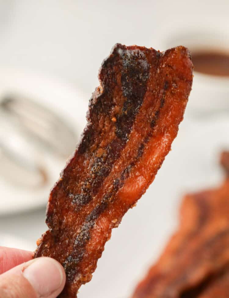 Picture of hand holding up a single piece of completed Smoked Candied Bacon.