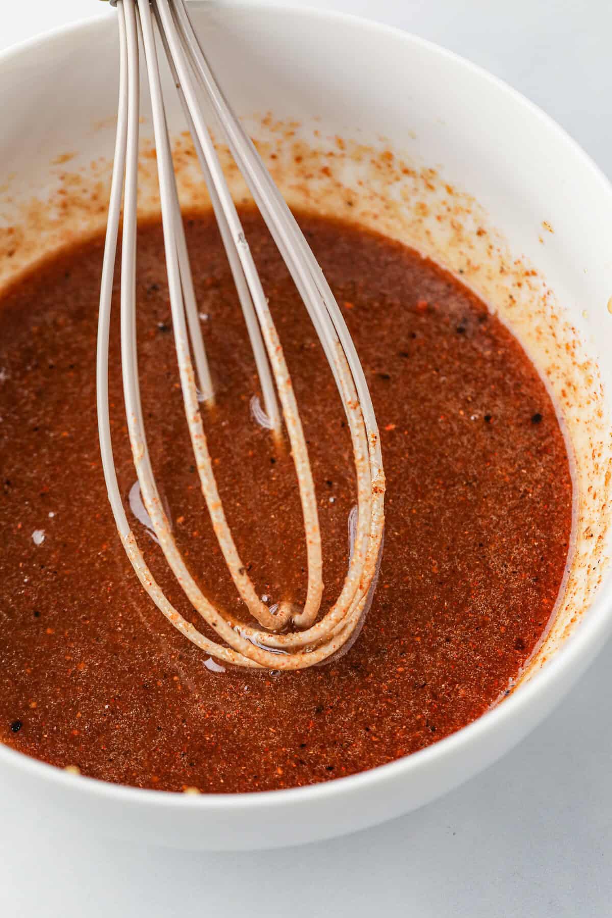 Close up image of white bowl with marinade and whisk in it.