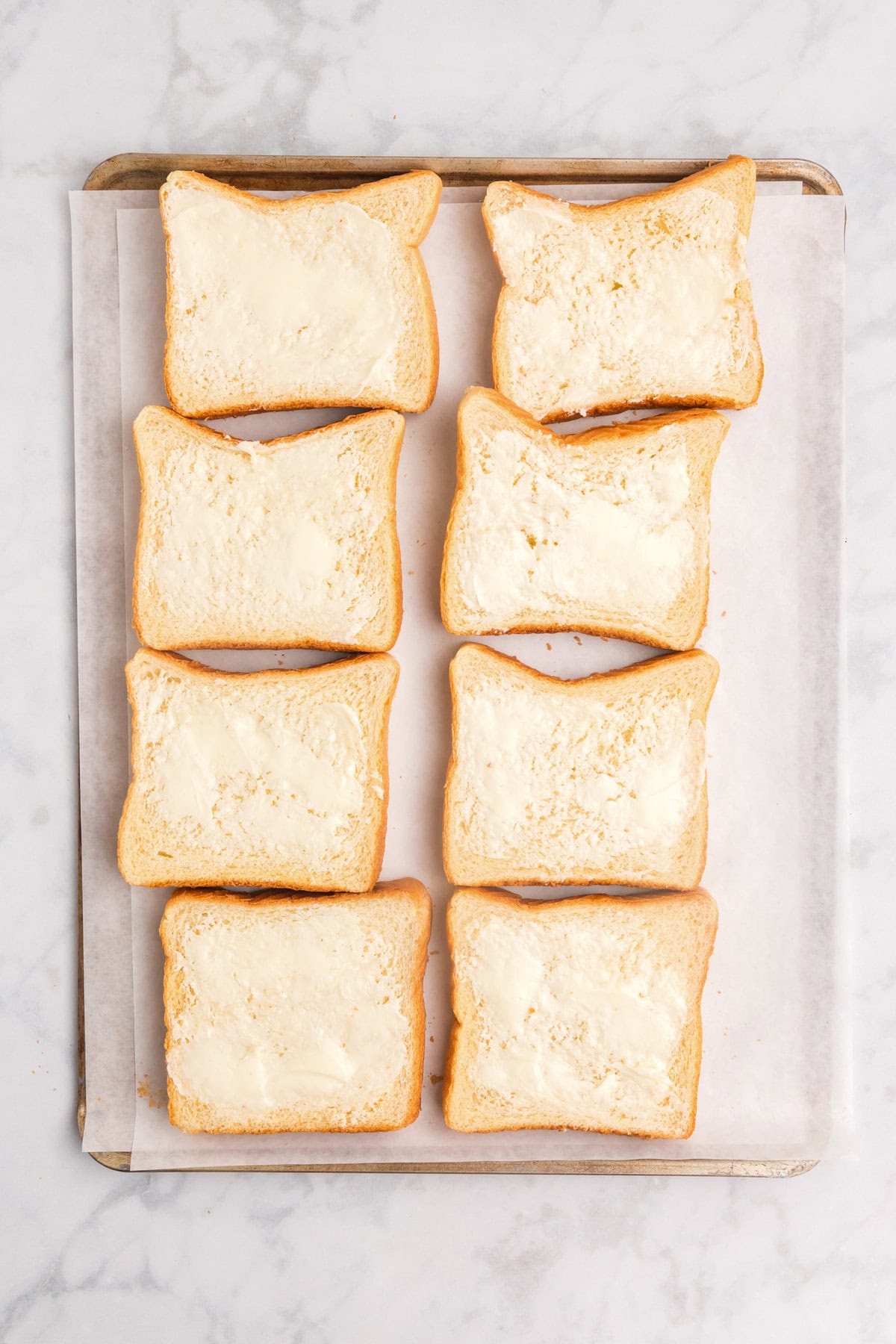 Overhead picture of 8 slices of buttered bread on parchment paper lined pan.