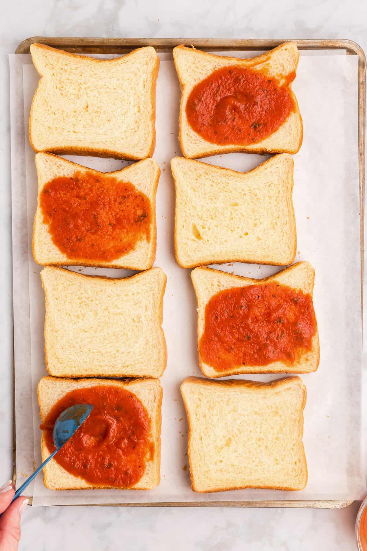 Overhead picture of 8 slices of bread with 4 of them that have pizza sauce on them.