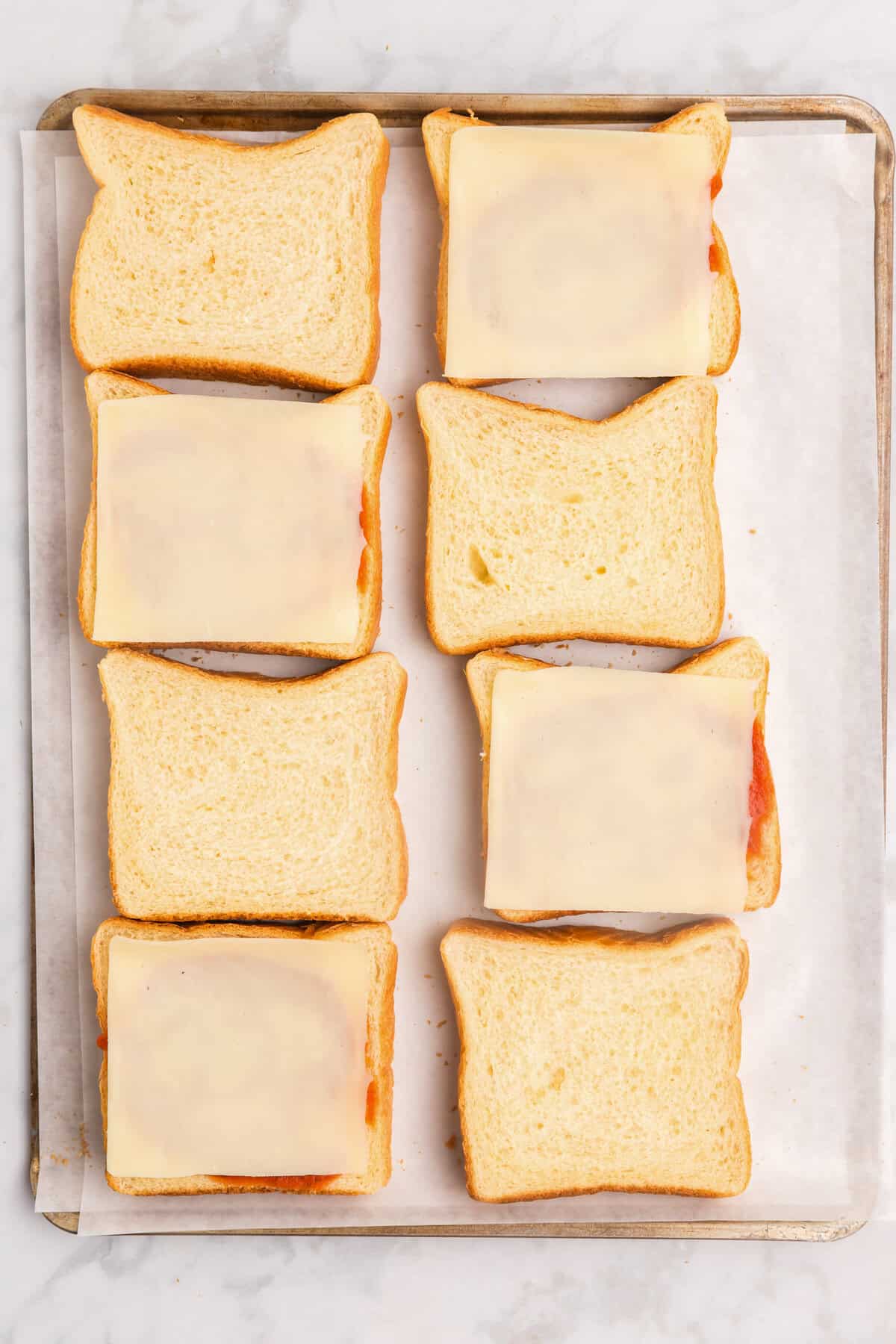 Overhead picture of 8 slices of bread with four of them that have pizza sauce and mozzarella cheese on them.