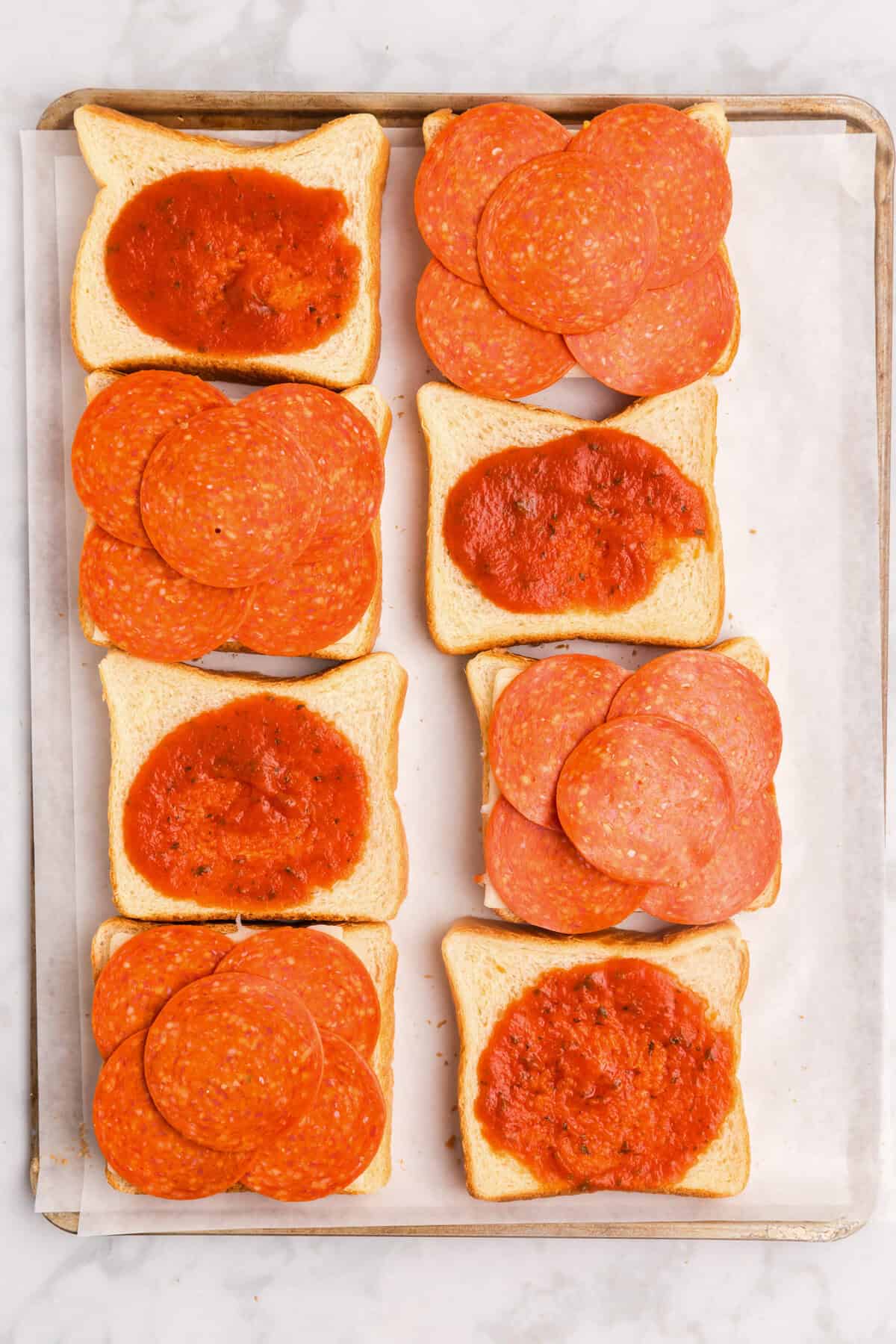 Overhead picture of 8 slices of bread with half with sauce on them and half with pepperoni on them.