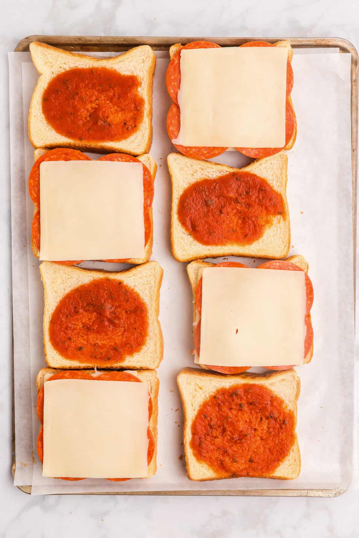 8 Slices of bread with half that have mozzarella layered ontop on pepperoni and the other half that have pizza sauce on them.
