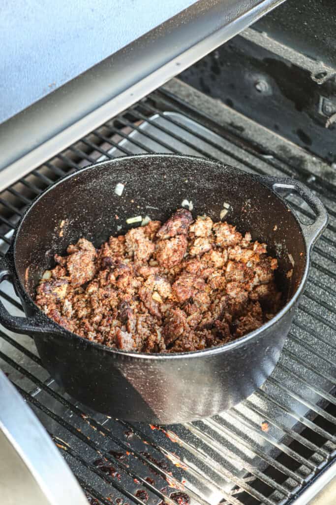 Side view picture of cooked ground beef in a cast iron pot on the smoker.