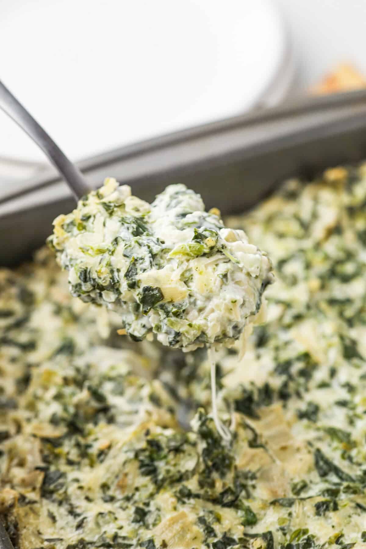 Cooked Smoked Spinach Artichoke Dip being scooped up by metal spoon. 