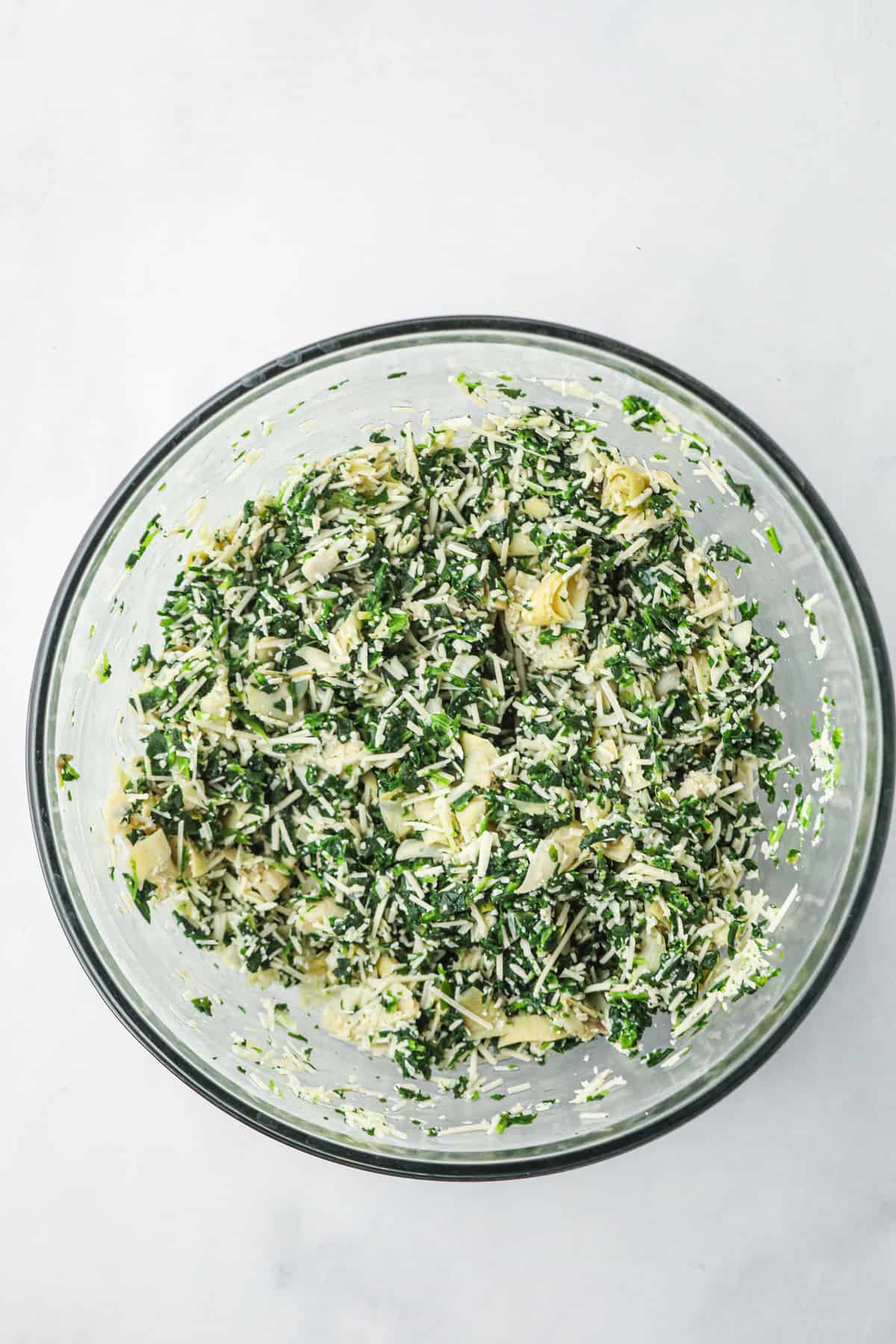 Overhead picture of Spinach Artichoke ingredients combined in a glass bowl.