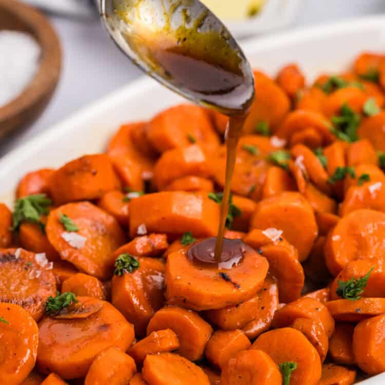 Close up of spoon drizzling glaze on carrots.