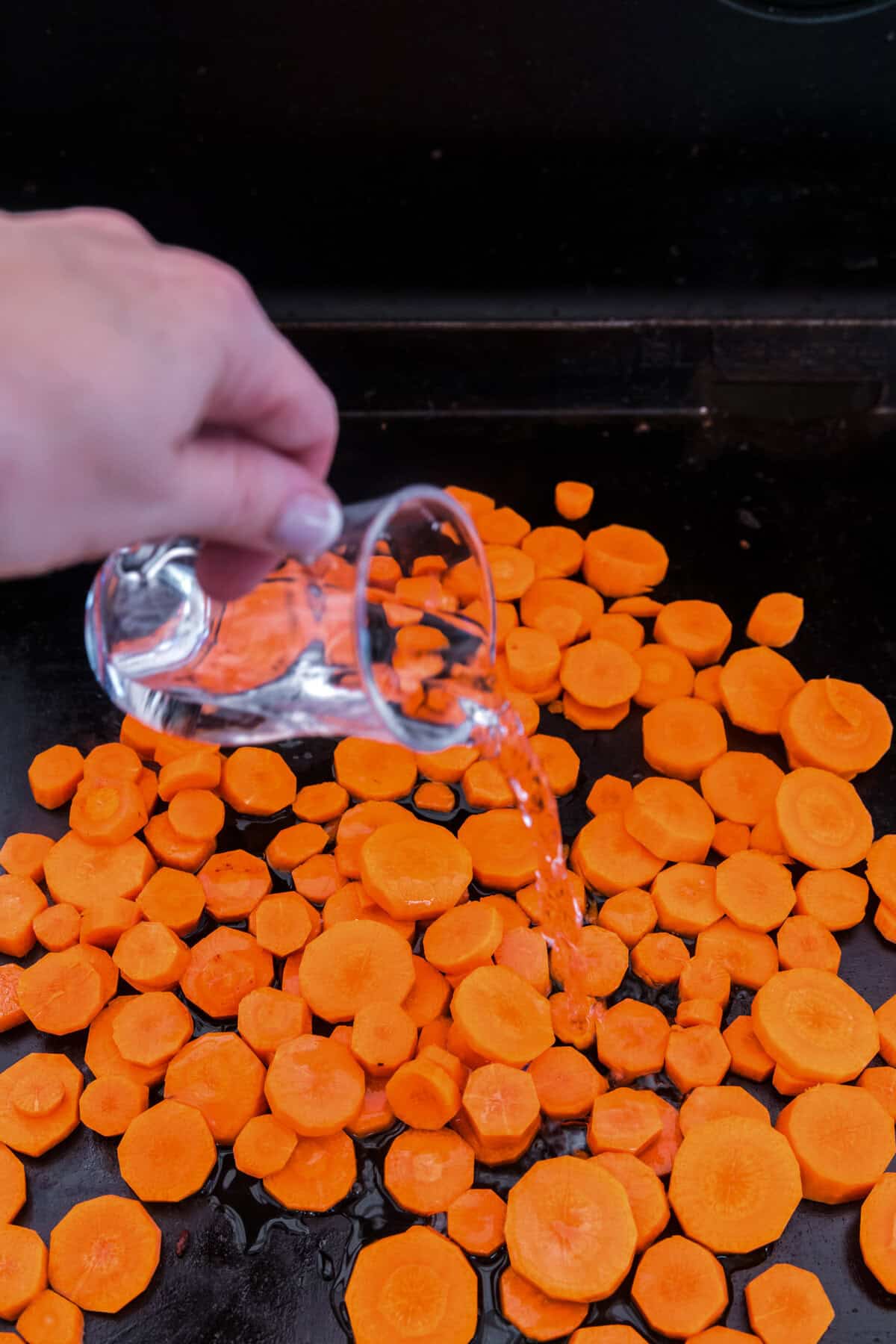 Close up image of water being poured onto carrots on the Blackstone.
