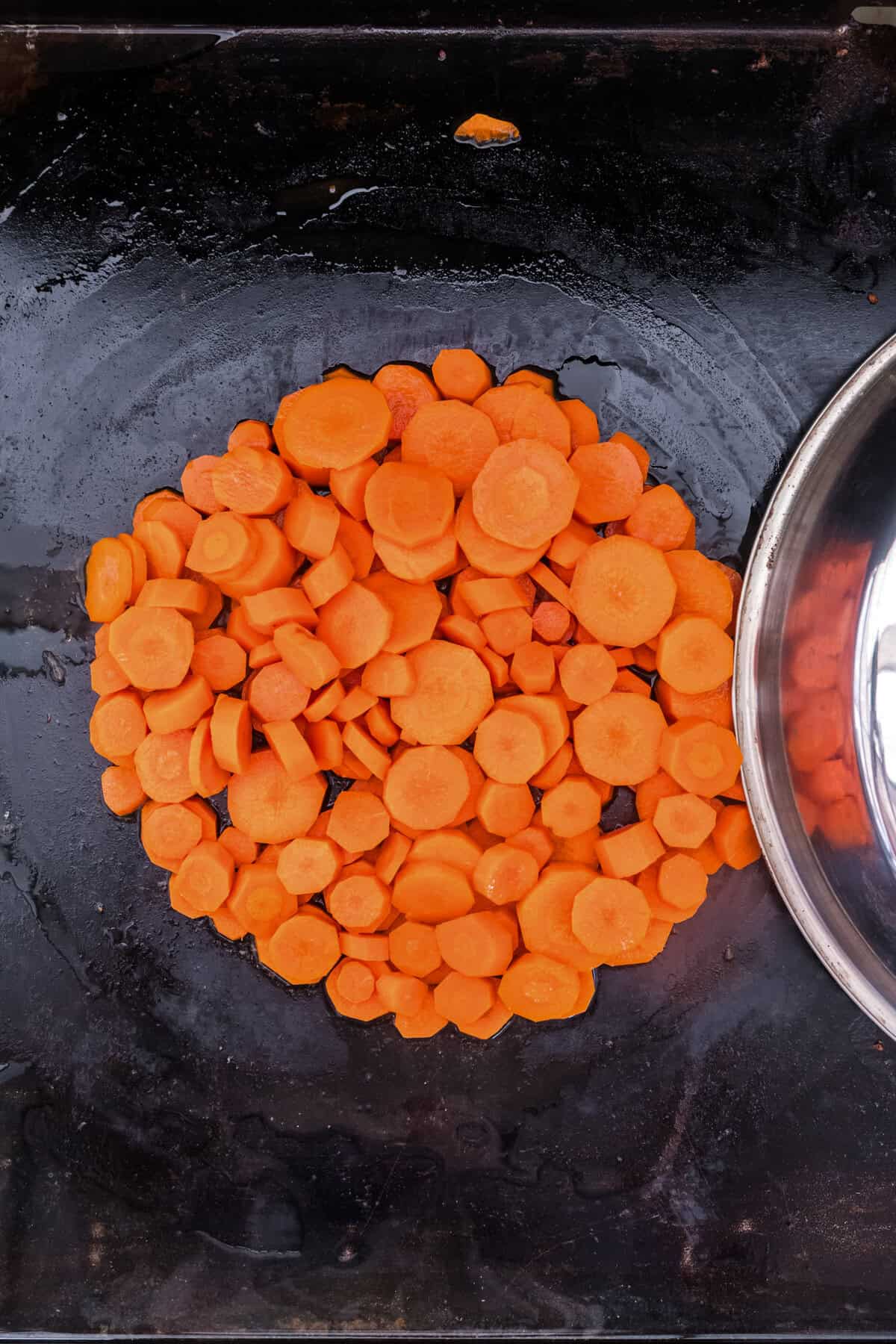 Overhead picture of food cover being removed from cooked carrots.