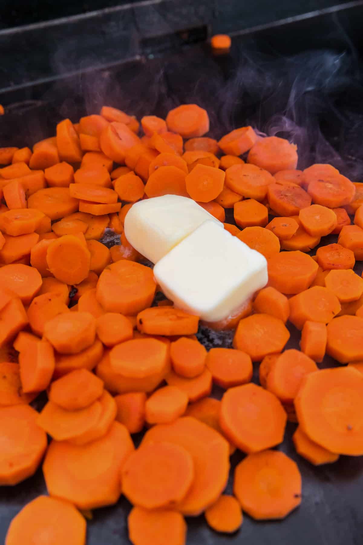 Close up picture of cooked carrots with 2 slices of butter unmelted on it.