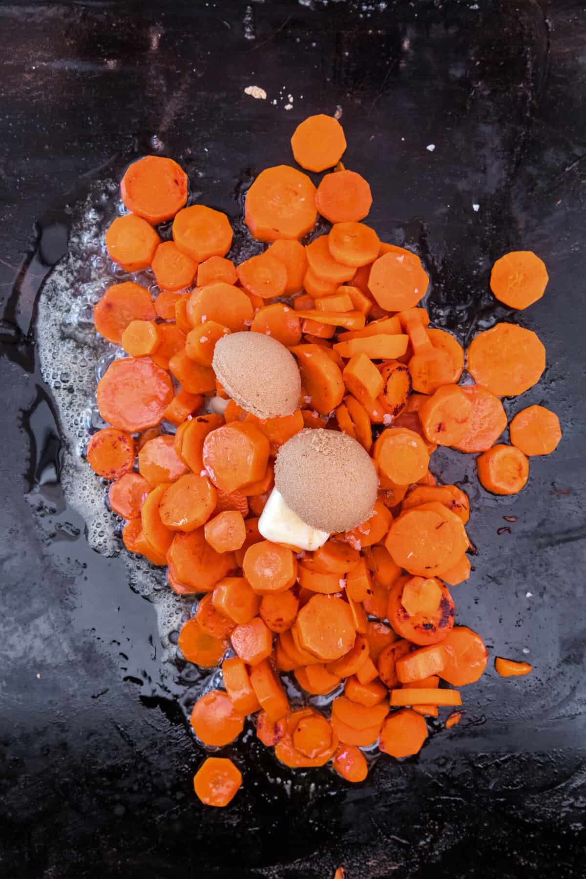 Overhead picture of cooked carrots with brown sugar and butter on top uncombined.