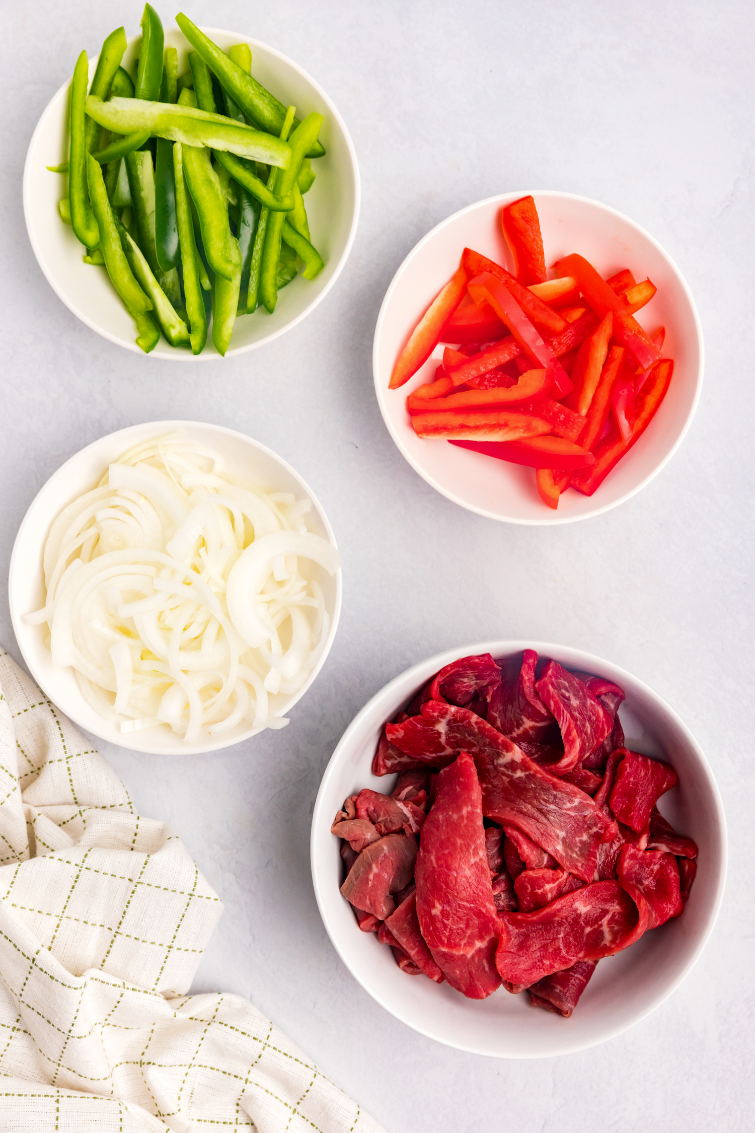 Overhead picture of raw steak, onions and peppers divided into separate bowls.