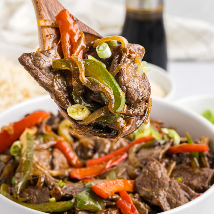 Picture of wooden spoon with blackstone pepper steak over a bowl filled with it.