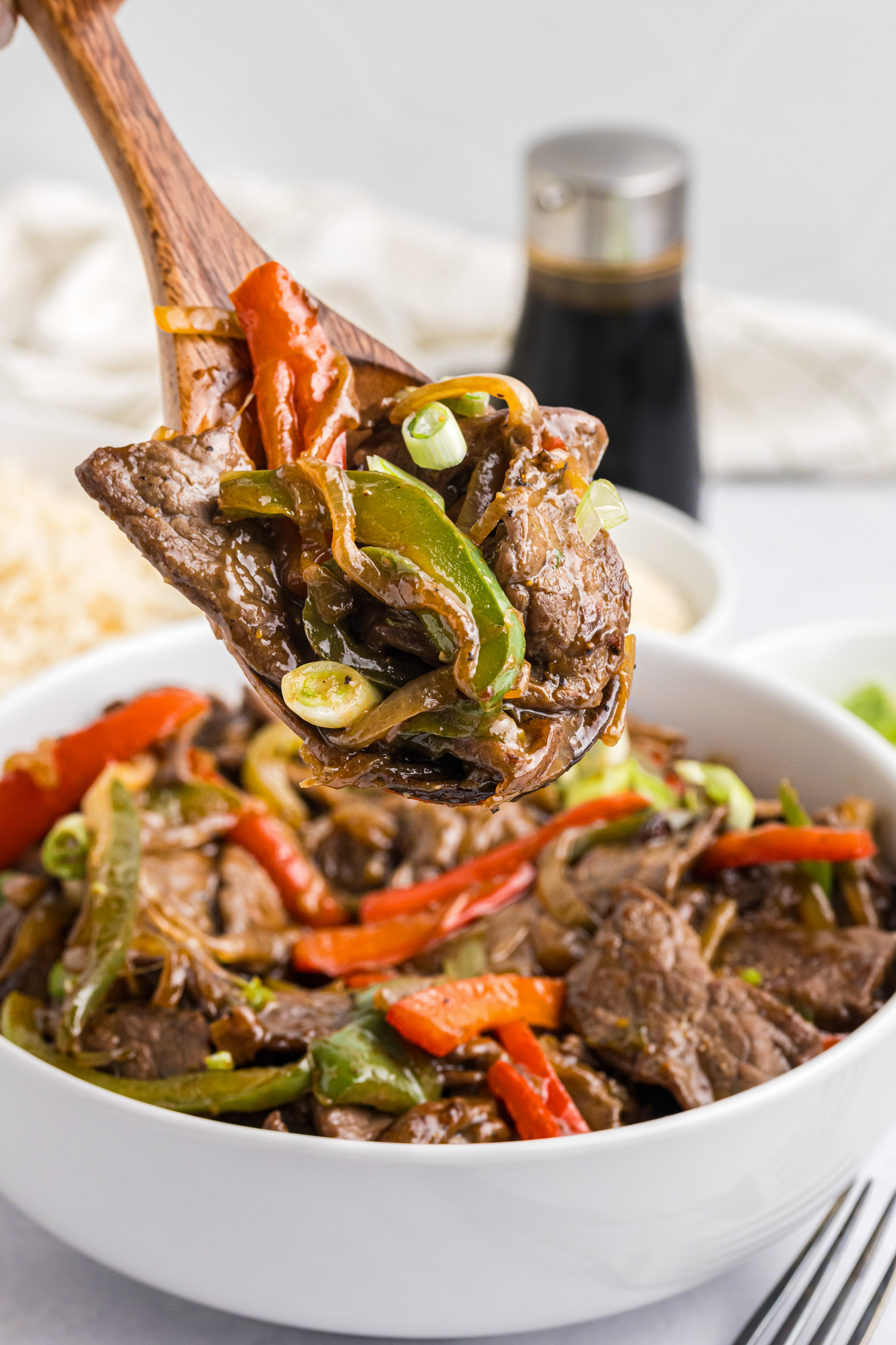 Picture of wooden spoon with blackstone pepper steak over a bowl filled with it.