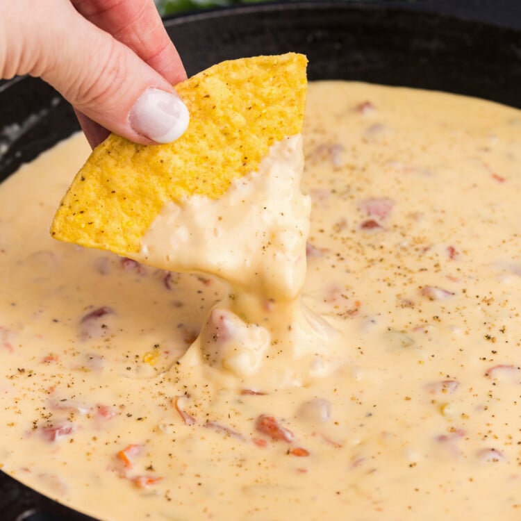 Side picture of hand holding a tortilla chip dipped in Blackstone Queso.