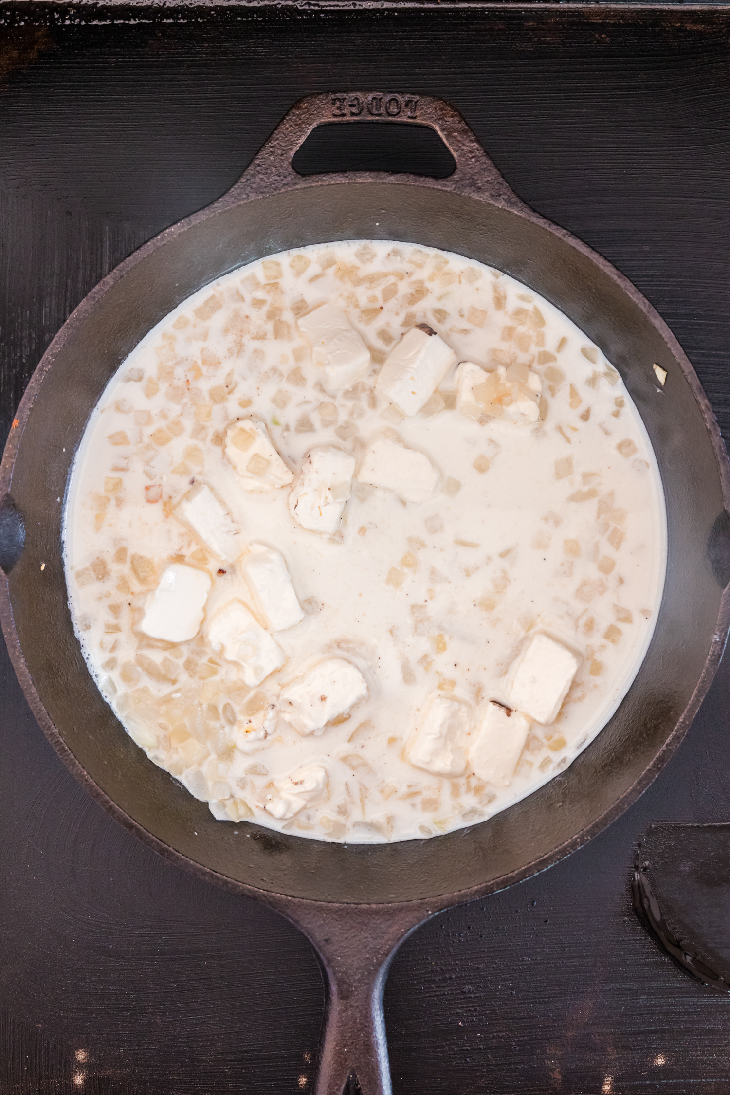 Overhead picture of milk, onions and cream cheese in a cast iron skillet.