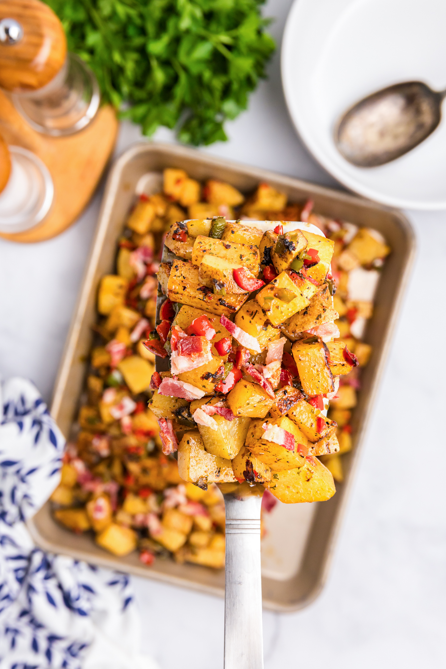 Spatula lifting a portion of Blackstone breakfast potatoes with crispy bacon and vegetables.