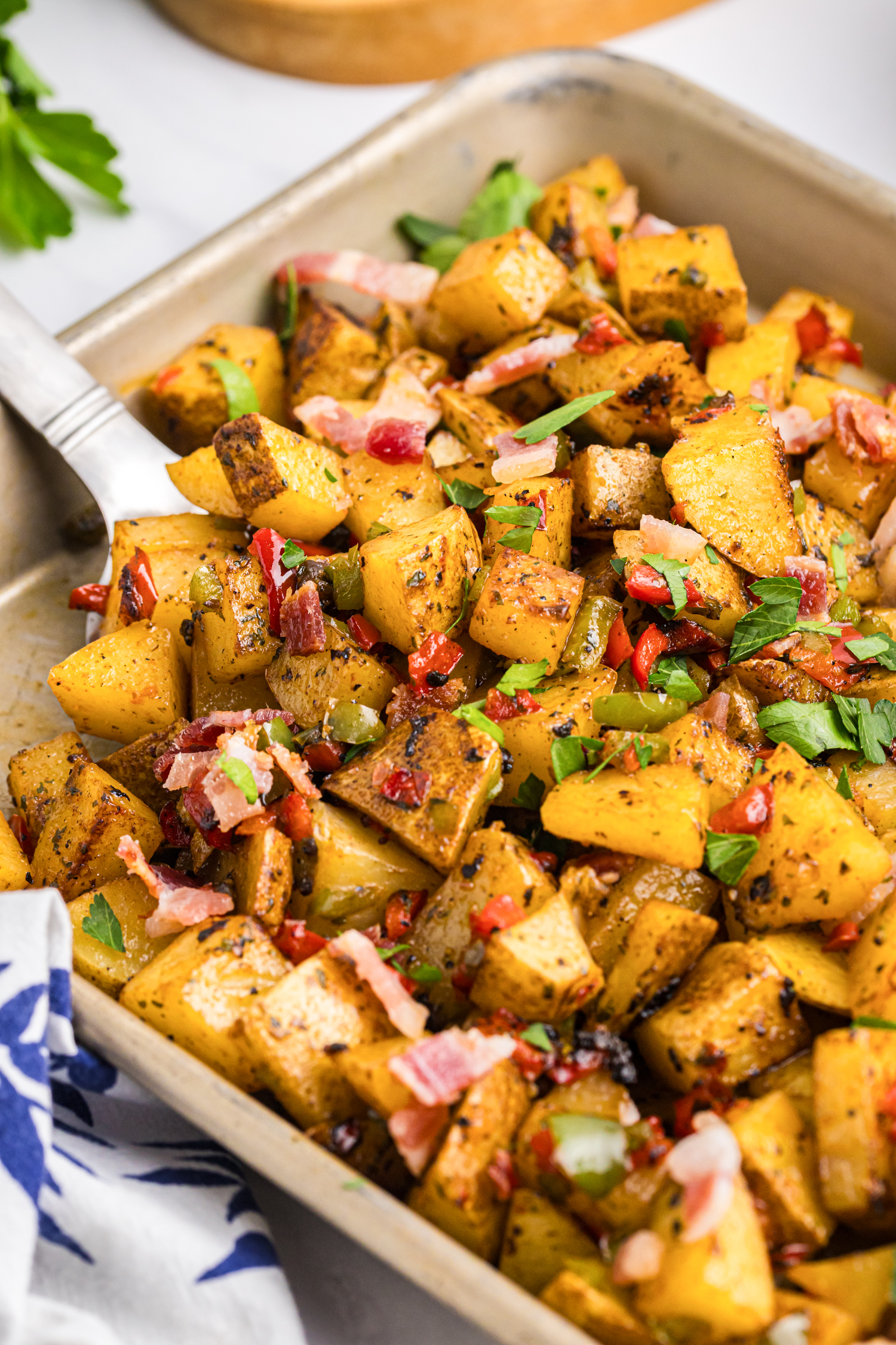 Cooked breakfast potatoes with bacon, peppers, and fresh parsley in a white bowl next to toast.