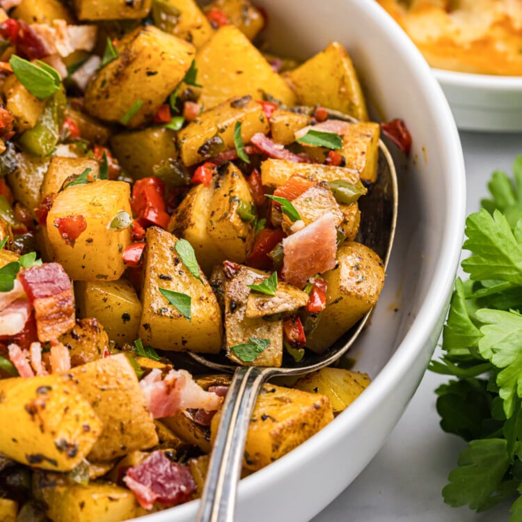 Top-down view of seasoned breakfast potatoes garnished with parsley and bacon in a white serving bowl.