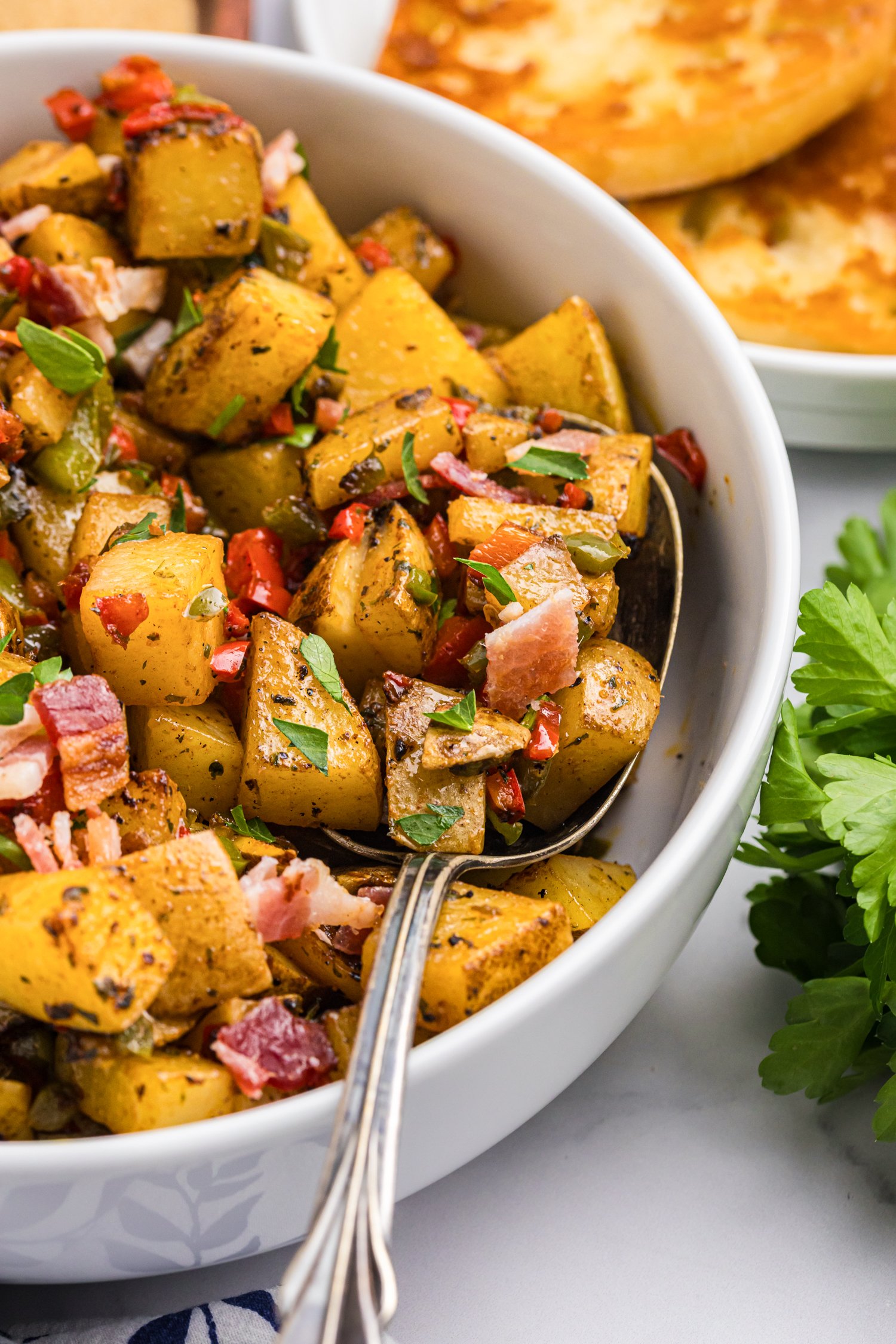 Top-down view of seasoned breakfast potatoes garnished with parsley and bacon in a white serving bowl.