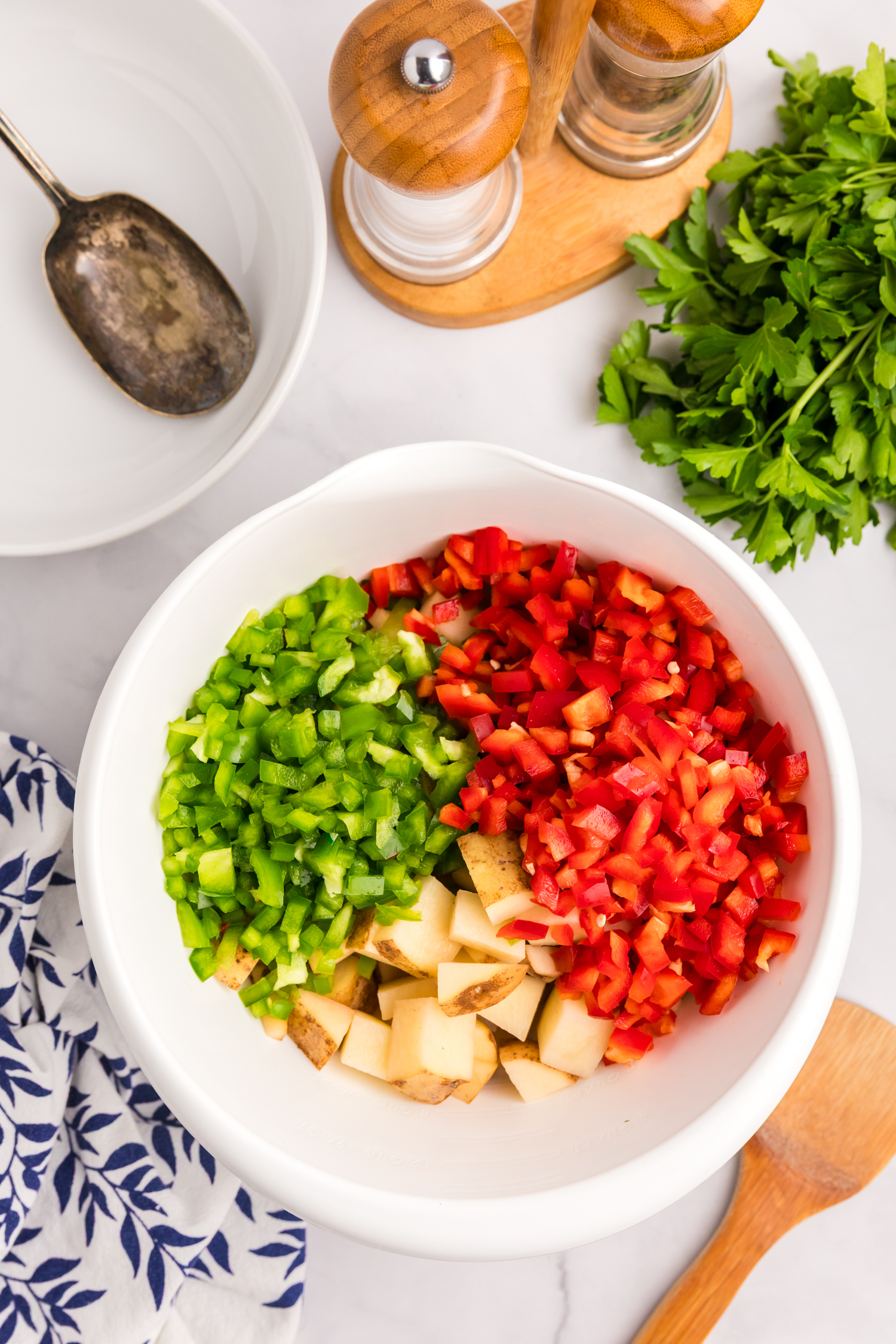 Chopped green bell pepper, red bell pepper, and cubed potatoes in a white mixing bowl.