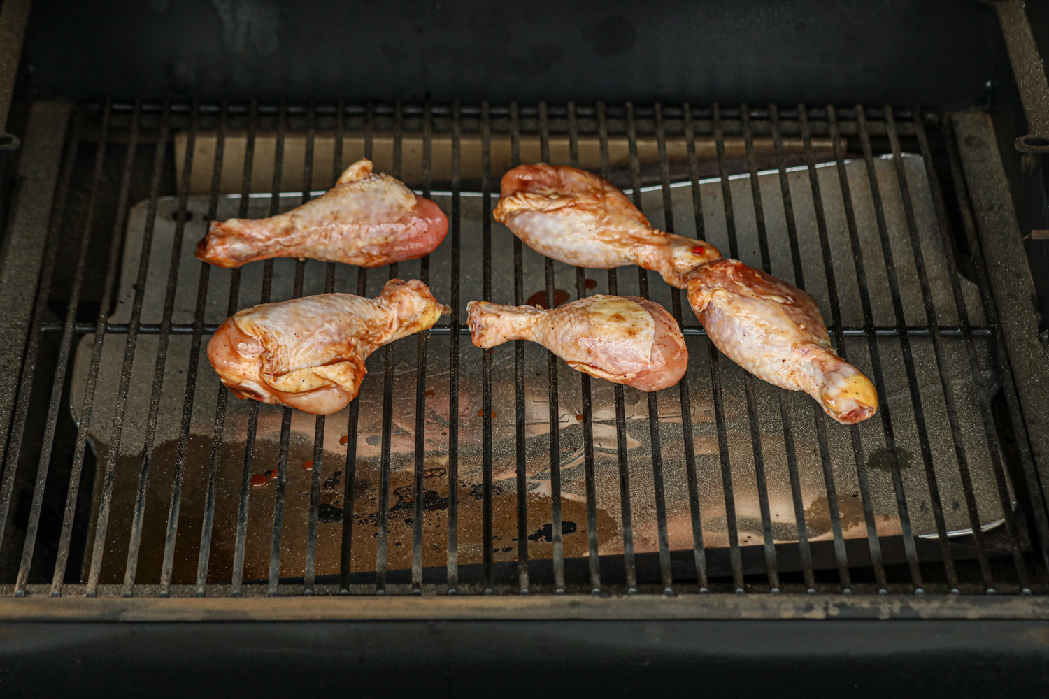 Raw marinated chicken drumsticks placed on a grill, ready to be cooked, with a background of grill grates and indirect heat zones visible below.