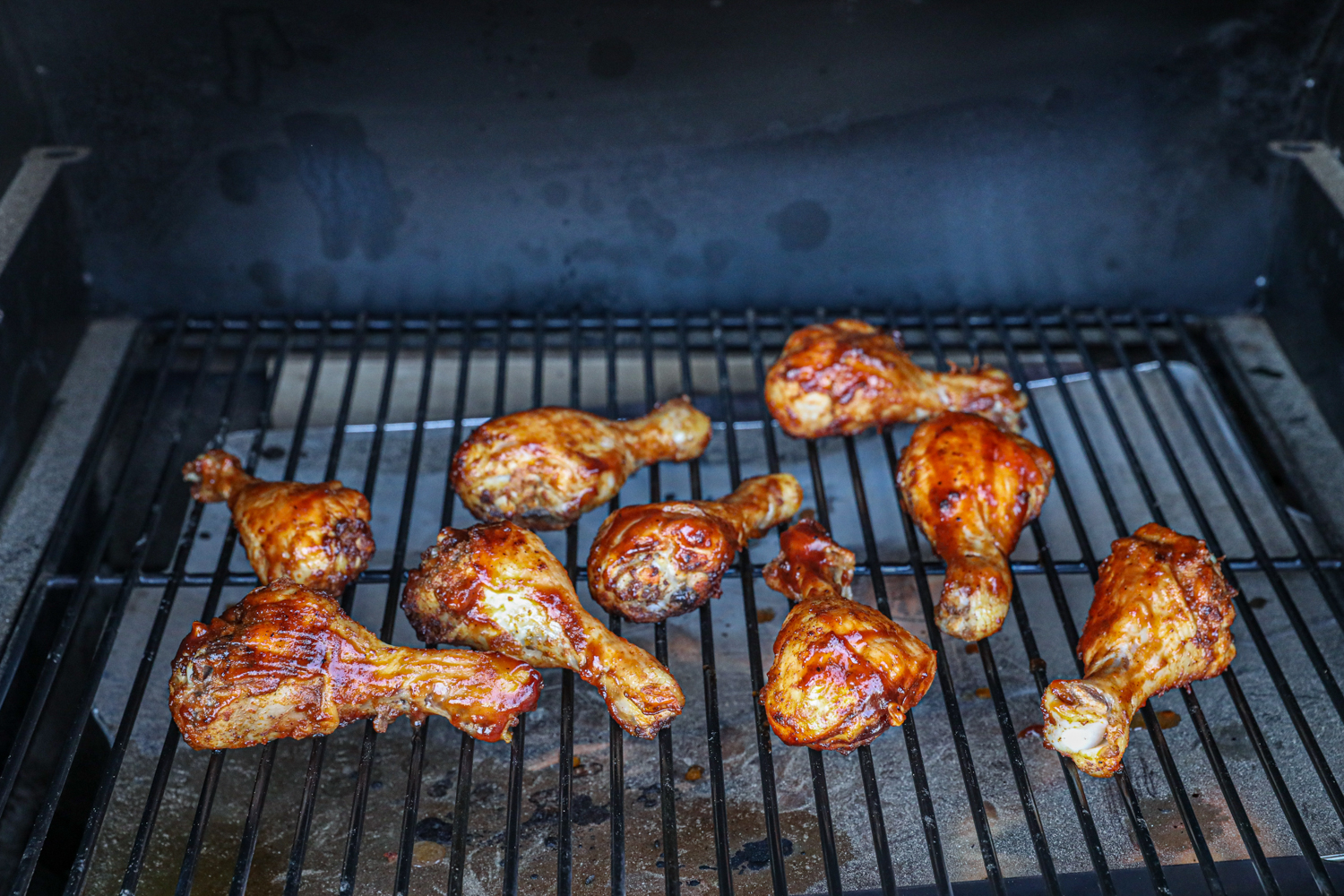 Chicken drumsticks on a grill, halfway through cooking, with a glossy coating of barbecue sauce caramelizing on the surface.