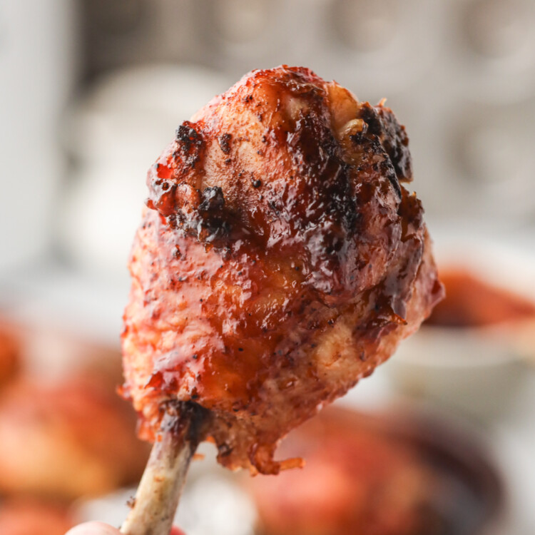 Close-up of a single smoked chicken lollipop held by the bone, showcasing its caramelized, saucy surface.