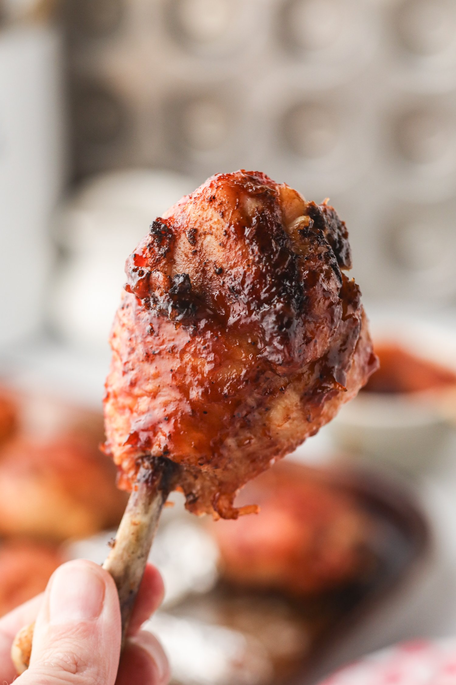 Close-up of a single smoked chicken lollipop held by the bone, showcasing its caramelized, saucy surface.
